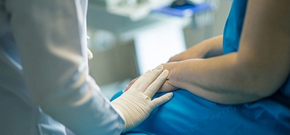 Ausschnitt der Hände von Arzt mit Kittel und weißem Handschuh sowie Assistenz in blauer OP Kleidung